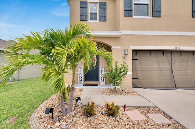 entrance to property with stucco siding, concrete driveway, a garage, and a yard
