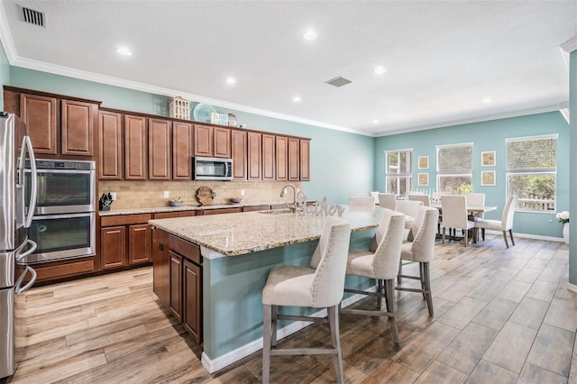 4094 Windcrest Dr, Wesley Chapel, FL 33544 - kitchen featuring light wood finished floors, a breakfast bar area, a sink, a kitchen island with sink, and appliances with stainless steel finishes