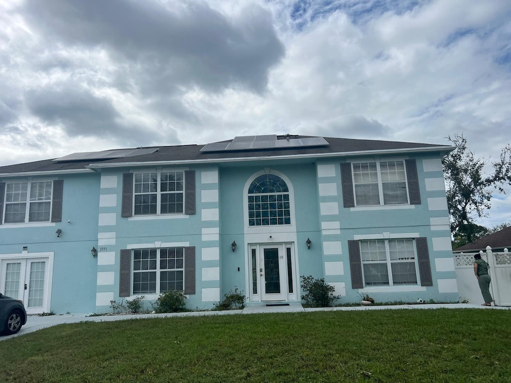 view of front of house featuring roof mounted solar panels, french doors, and a front yard
