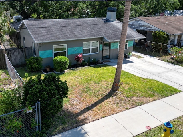 ranch-style house featuring a front lawn, stucco siding, roof with shingles, and fence