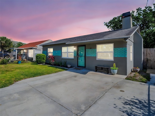 ranch-style home featuring roof with shingles, fence, stucco siding, a chimney, and a lawn