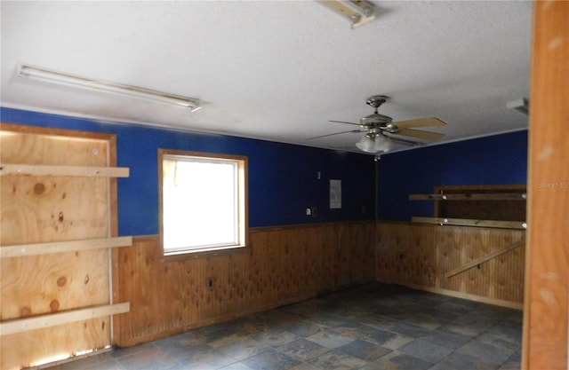 empty room featuring a ceiling fan, wooden walls, and a wainscoted wall