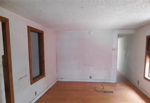 spare room with a textured ceiling, visible vents, and wood finished floors