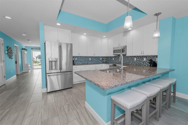 kitchen with a peninsula, decorative backsplash, stainless steel appliances, and white cabinetry