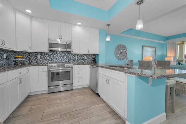 kitchen with a sink, a peninsula, stainless steel appliances, tasteful backsplash, and white cabinetry