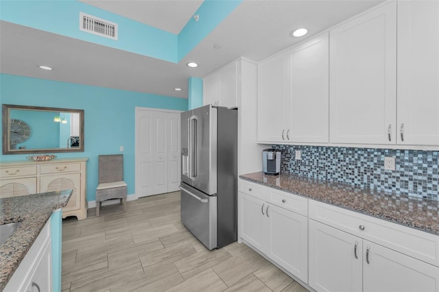 kitchen featuring white cabinetry, stainless steel fridge with ice dispenser, dark stone countertops, and visible vents