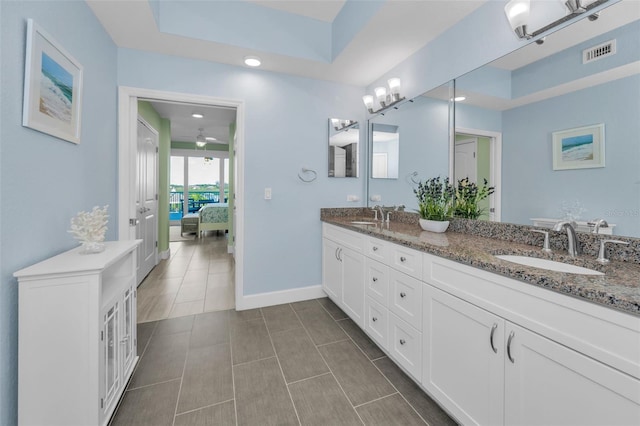 ensuite bathroom with a tray ceiling, double vanity, visible vents, and a sink