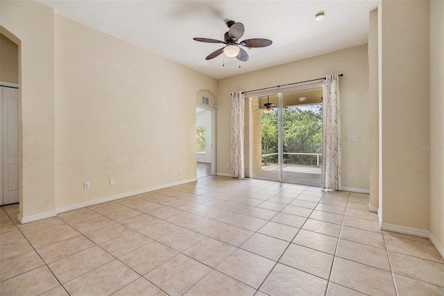 empty room with baseboards, light tile patterned flooring, ceiling fan, and arched walkways