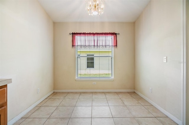 empty room featuring an inviting chandelier, baseboards, light tile patterned floors, and plenty of natural light