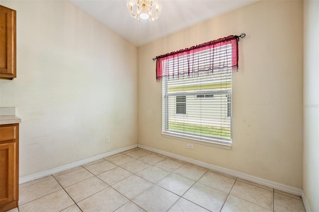 unfurnished dining area featuring an inviting chandelier, light tile patterned flooring, and baseboards