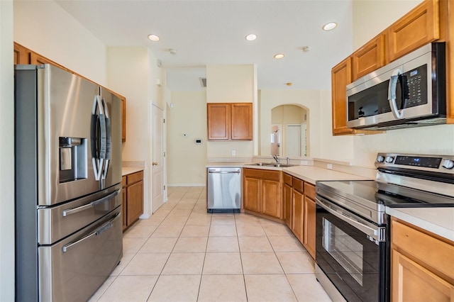 kitchen featuring brown cabinets, a sink, arched walkways, light countertops, and appliances with stainless steel finishes