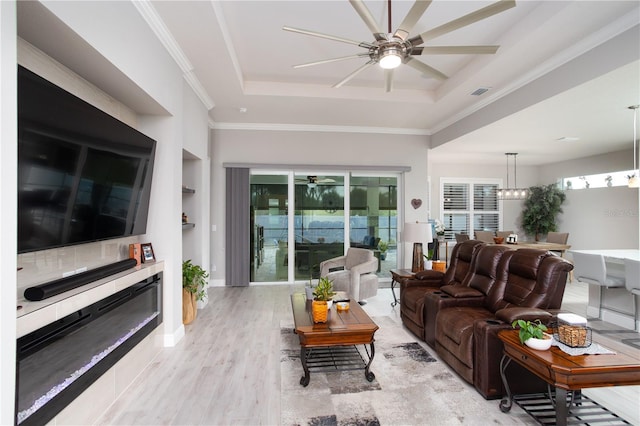 living room featuring a tray ceiling, ceiling fan, light wood-type flooring, built in features, and ornamental molding