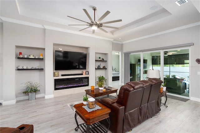 living area with ceiling fan, a tray ceiling, wood finished floors, and ornamental molding