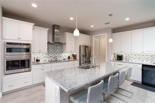 kitchen featuring wall chimney range hood, stainless steel appliances, a sink, beverage cooler, and backsplash