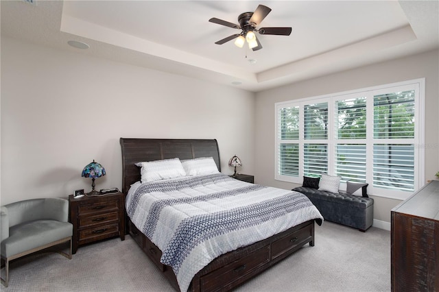 bedroom featuring a tray ceiling, light carpet, a ceiling fan, and baseboards