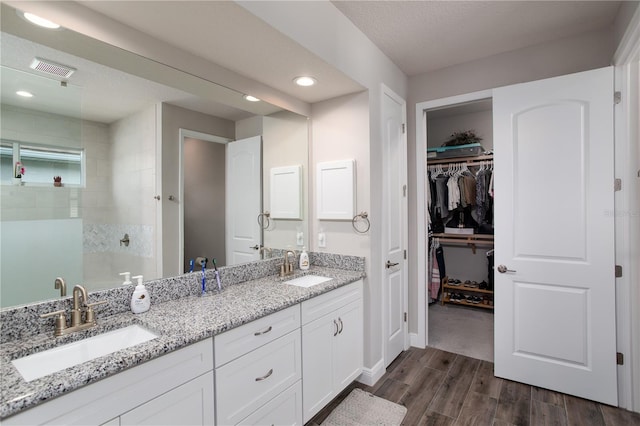 full bathroom with wood finished floors, tiled shower, a spacious closet, double vanity, and recessed lighting