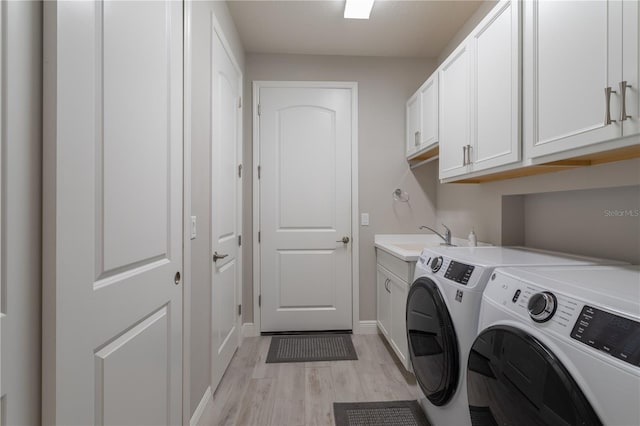 clothes washing area with washing machine and dryer, light wood finished floors, cabinet space, and baseboards