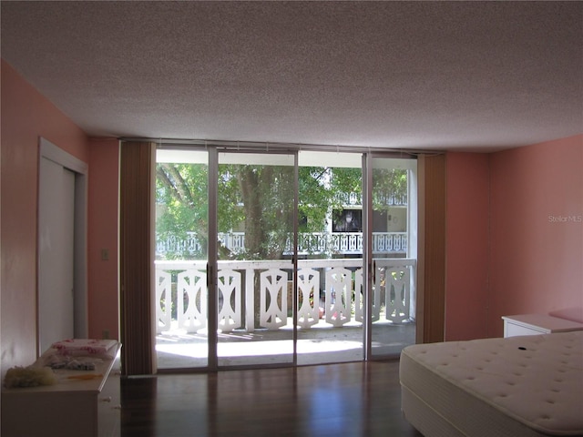 bedroom with access to exterior, a textured ceiling, expansive windows, and wood finished floors