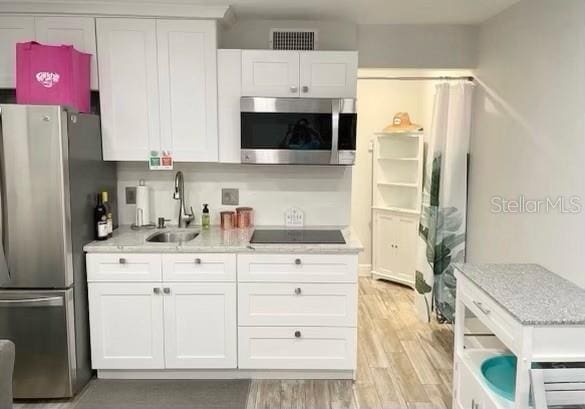 kitchen featuring light wood-type flooring, white cabinets, appliances with stainless steel finishes, and a sink