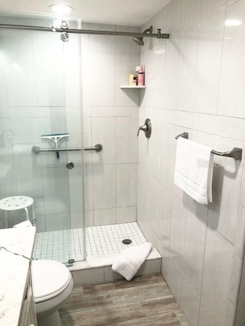 bathroom with toilet, tile walls, a shower stall, and wood finished floors