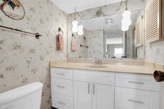 bathroom featuring toilet, vanity, and wallpapered walls