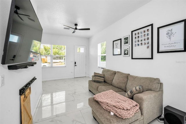 living room with a ceiling fan, marble look tile flooring, plenty of natural light, and baseboards