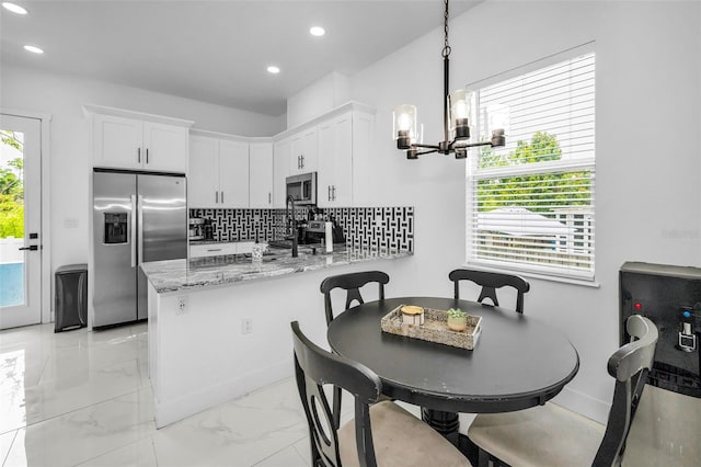 kitchen featuring appliances with stainless steel finishes, a chandelier, a peninsula, light marble finish floors, and white cabinetry