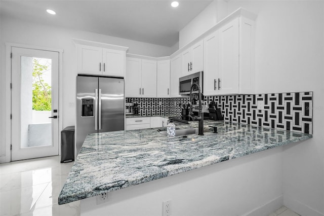 kitchen featuring appliances with stainless steel finishes, light stone counters, a peninsula, decorative backsplash, and white cabinetry