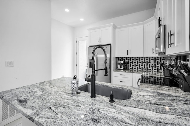 kitchen featuring a sink, light stone counters, white cabinetry, stainless steel microwave, and tasteful backsplash