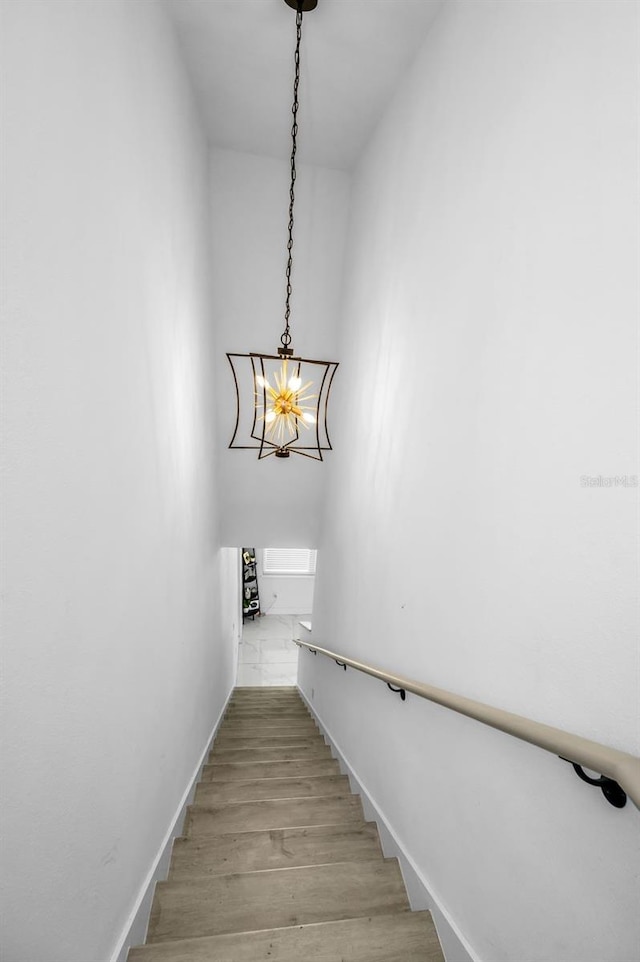stairway featuring wood finished floors, baseboards, and a chandelier