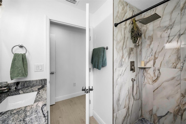 full bath with wood finished floors, a marble finish shower, vanity, and baseboards
