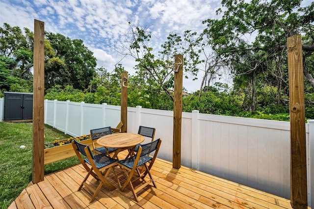 wooden deck featuring outdoor dining area, fence, a storage shed, an outdoor structure, and view of wooded area