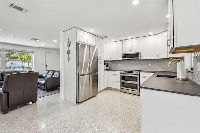 kitchen with appliances with stainless steel finishes, dark countertops, open floor plan, white cabinets, and tasteful backsplash