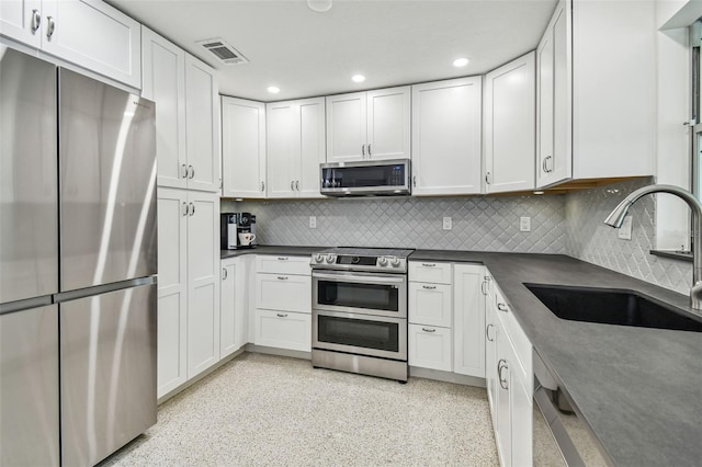 kitchen featuring stainless steel appliances, a sink, dark countertops, recessed lighting, and white cabinetry