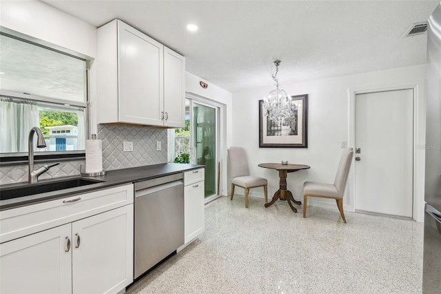 kitchen with stainless steel dishwasher, dark countertops, dark aggregate flooring, a chandelier, and a sink