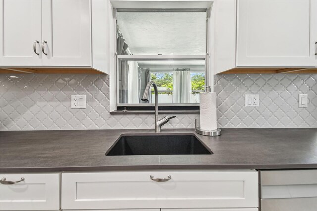 kitchen with dark countertops, a sink, tasteful backsplash, and white cabinets