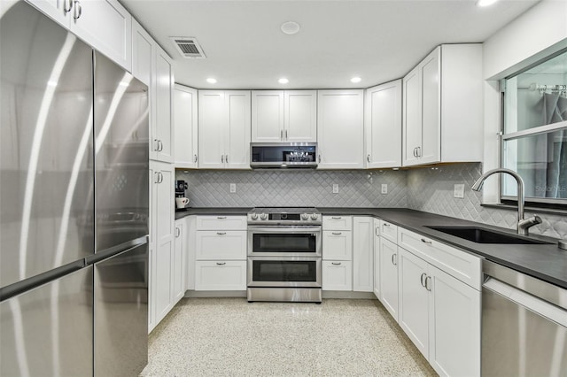kitchen featuring appliances with stainless steel finishes, a sink, dark countertops, recessed lighting, and decorative backsplash