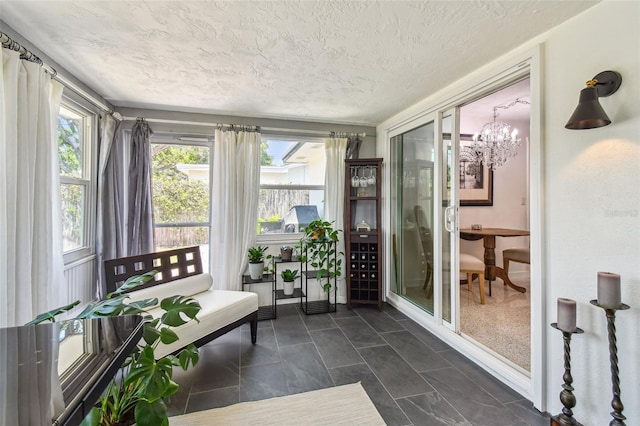sunroom / solarium with plenty of natural light, a textured ceiling, a chandelier, and baseboards