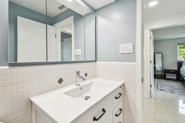 ensuite bathroom featuring tile walls, vanity, a wainscoted wall, and speckled floor