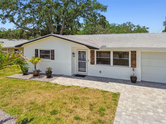 ranch-style house with brick siding, a front lawn, a shingled roof, and an attached garage
