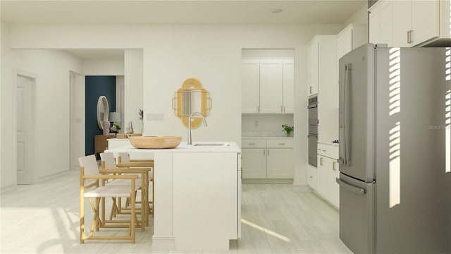 kitchen featuring freestanding refrigerator, a sink, white cabinetry, double oven, and an island with sink
