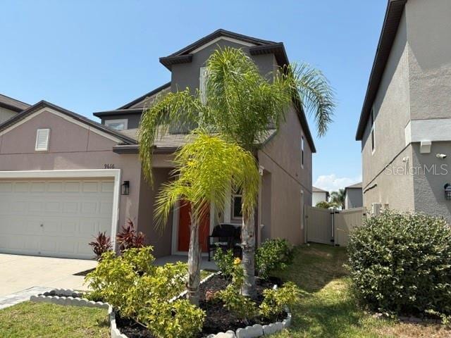 traditional-style home featuring driveway, stucco siding, an attached garage, and a gate