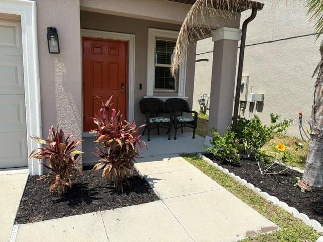 doorway to property with stucco siding, covered porch, and a garage