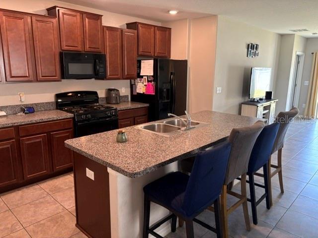 kitchen featuring a sink, a breakfast bar, black appliances, and light tile patterned floors
