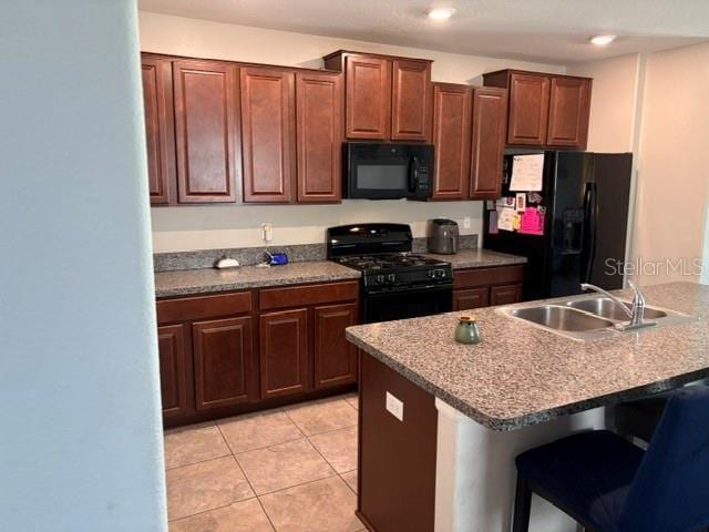 kitchen with light tile patterned floors, a kitchen breakfast bar, black appliances, and a sink