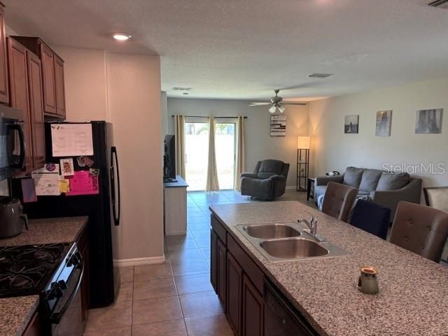 kitchen featuring light tile patterned floors, black appliances, open floor plan, and a sink