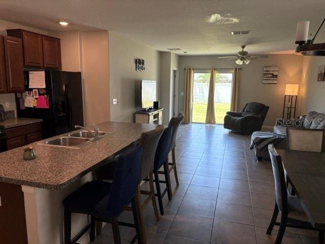 kitchen featuring a sink, a breakfast bar area, black refrigerator with ice dispenser, ceiling fan, and open floor plan
