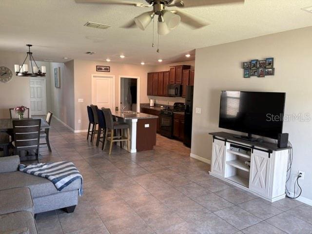 living room featuring baseboards, light tile patterned floors, recessed lighting, and ceiling fan with notable chandelier