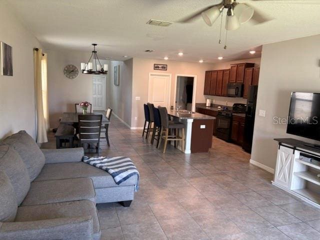 living room featuring ceiling fan with notable chandelier, visible vents, baseboards, light tile patterned flooring, and recessed lighting