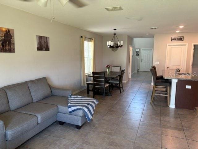 living room with ceiling fan with notable chandelier, baseboards, light tile patterned floors, and visible vents